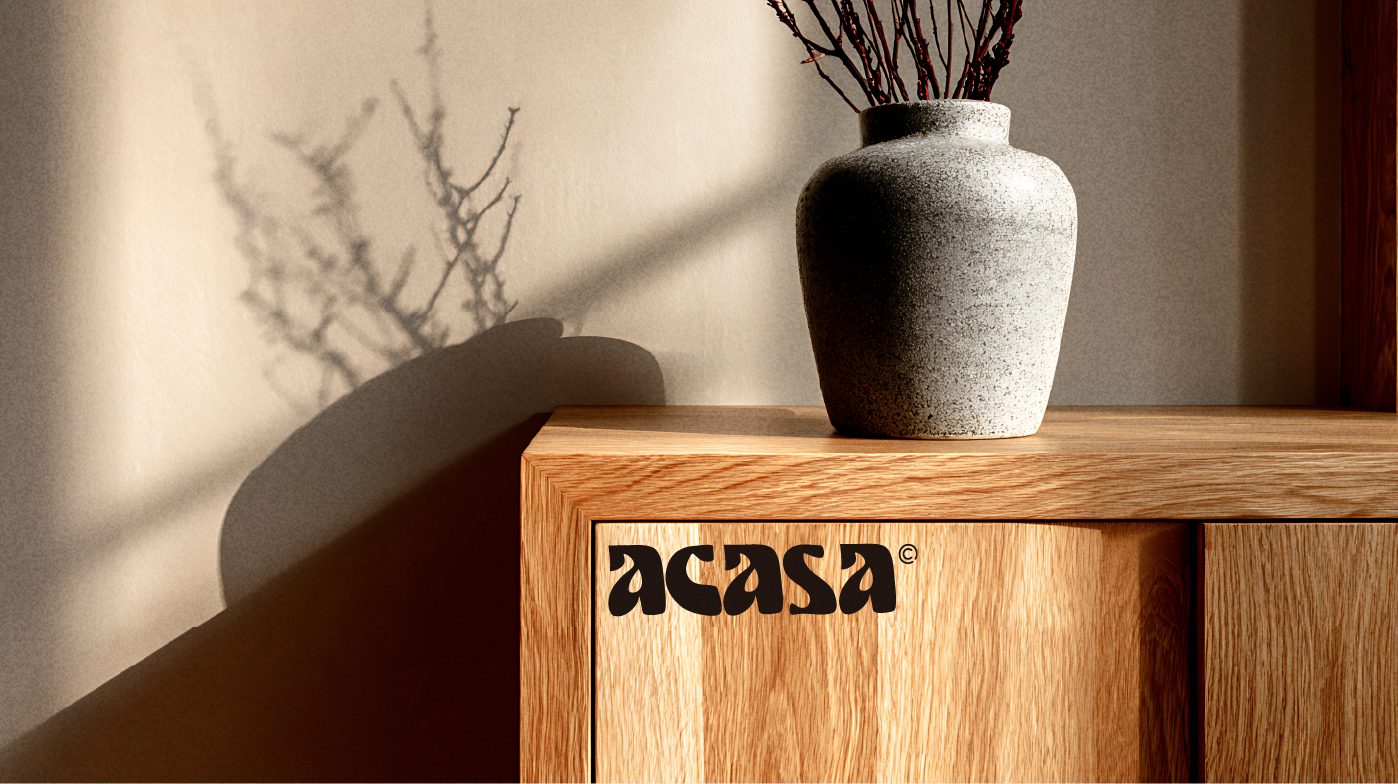 Mise en situation Acasa — wordmark gravé sur un meuble en chêne, vase et lumière rasante